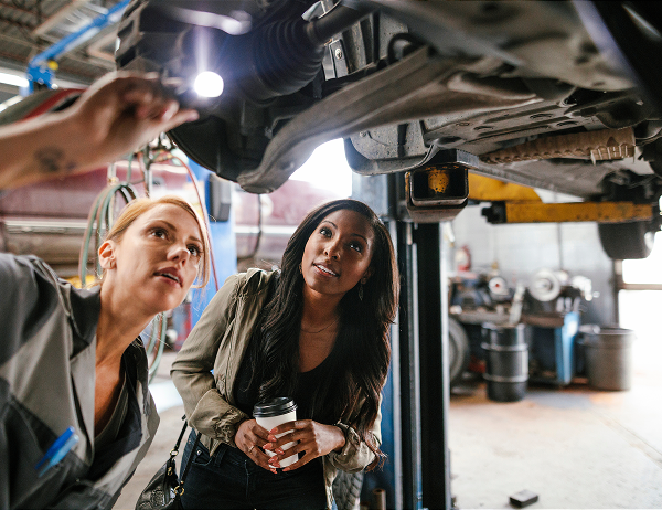 Mechanic under car on lift with female customer in garage